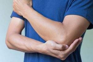 Массирует локоть на ручке Массирует локоть на руке